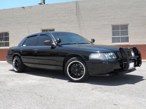 2003 Ford Crown Victoria - Lowered black Crown Victoria shown front left with push bar, black grille and headlights on.