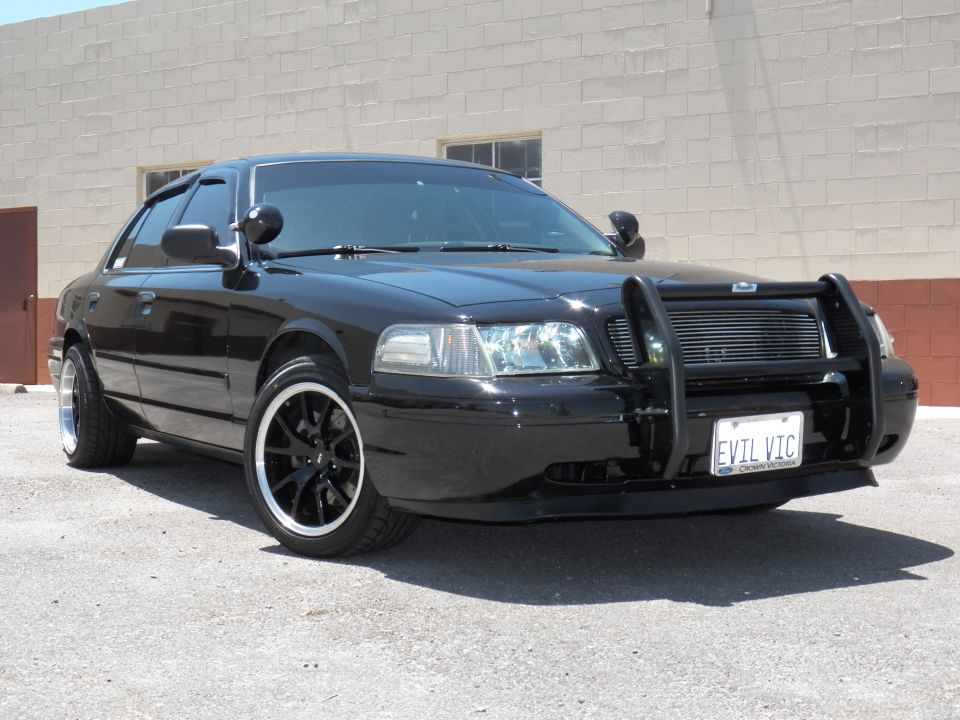 Black Ford Crown Victoria with push bar parked by a brick wall