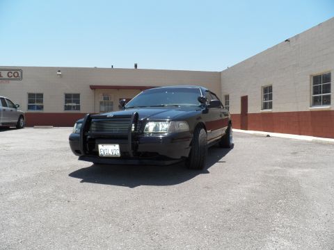 2003 Ford Crown Victoria - Three-quarter front angle of a black Crown Victoria sedan parked outside a tan industrial building.