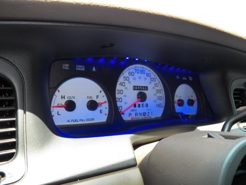 2003 Ford Crown Victoria - Wider dash view showing blue-glowing gauges, air vent and steering wheel in a tan-trimmed cabin.