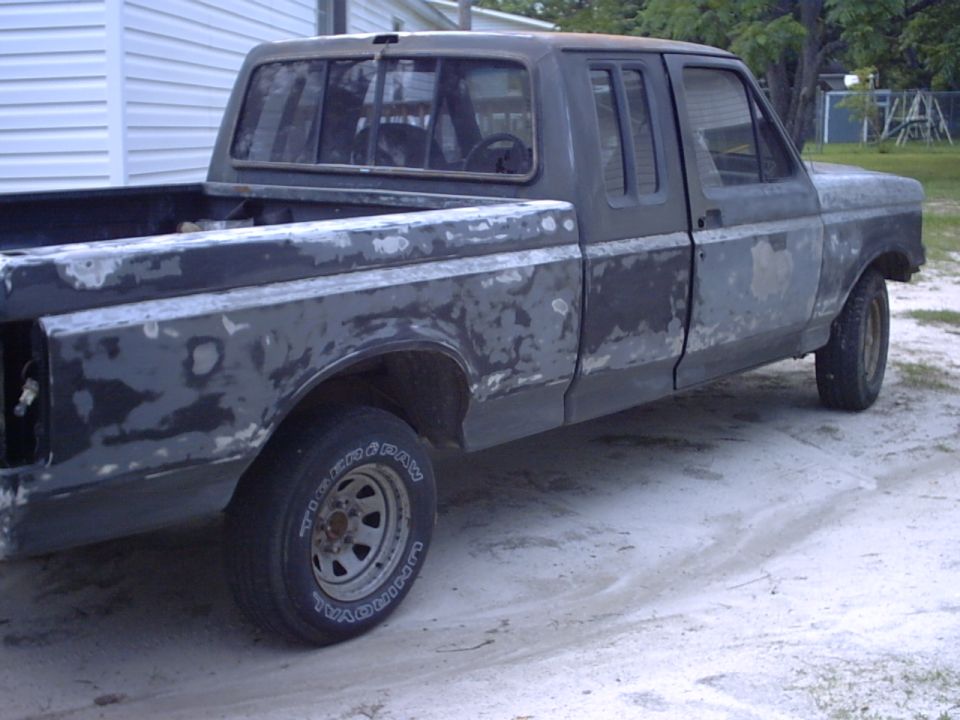 Side view of a 1989 Ford F-150 pickup truck in primer, undergoing body work