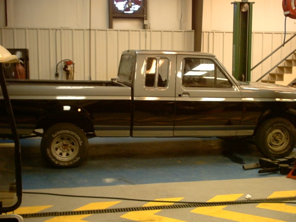 Two-tone gray and black Ford F-150 pickup truck, side view, in a garage