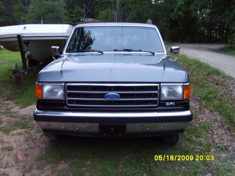 1989 Ford F-150 - This Ford F-Series truck has a chrome bumper and a grille with the Ford logo. A boat on a trailer is visible behind it.