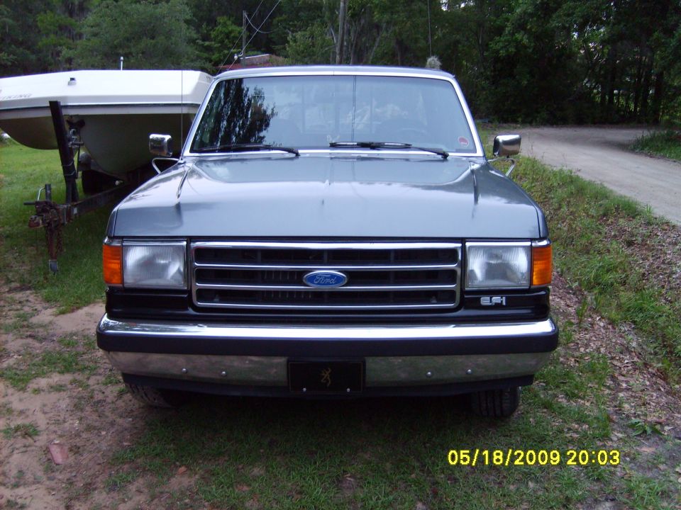 Front view of a gray Ford F-Series truck, parked outside with a boat on a trailer behind it