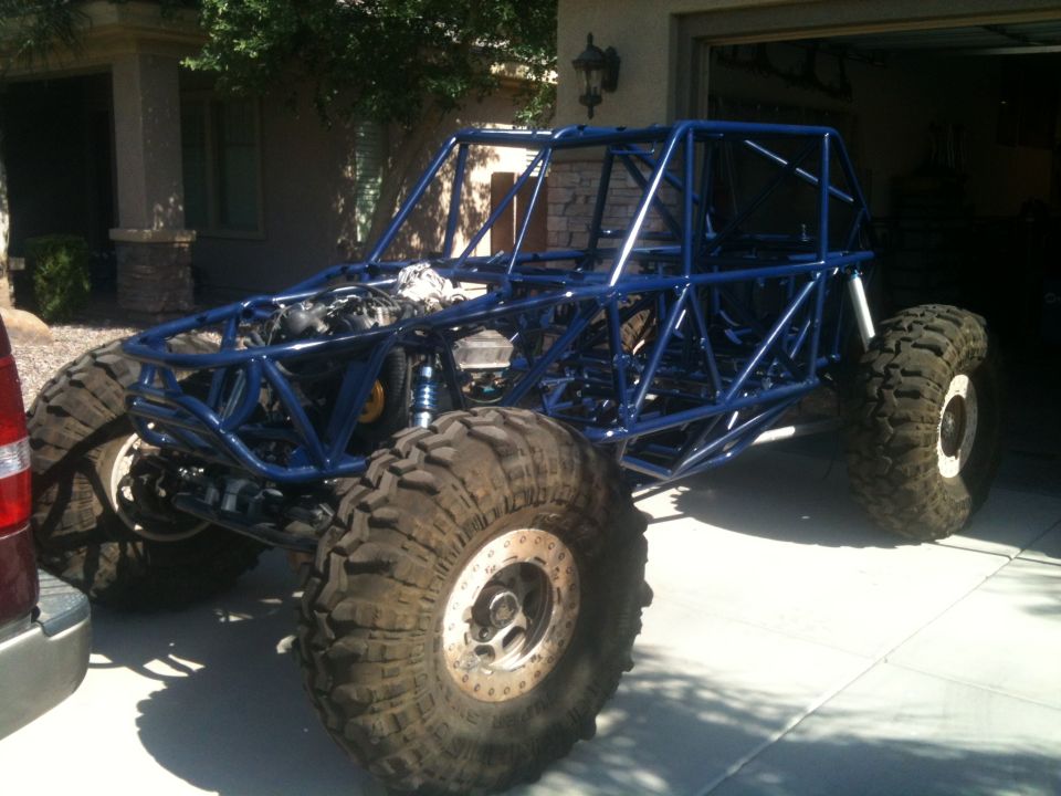 Blue tube frame off-road buggy with large tires and exposed engine, parked in a driveway