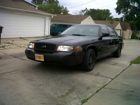 1999 Ford Crown Victoria - A black sedan is parked in a driveway with a garage in the background. The license plate is visible.