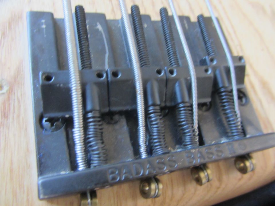 Close-up of a bass guitar bridge with five strings and "BADASS BASS CO" engraved on it