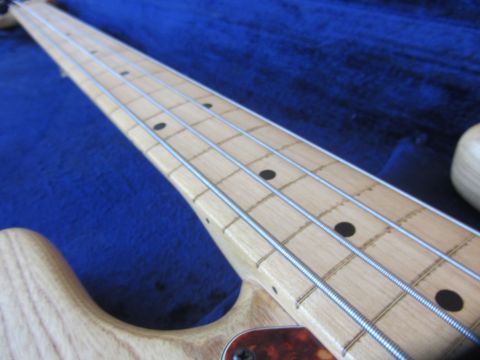 1968 Ford Mustang - Detail of a bass guitar neck, showing the fretboard, strings, and tuning pegs against a blue background.