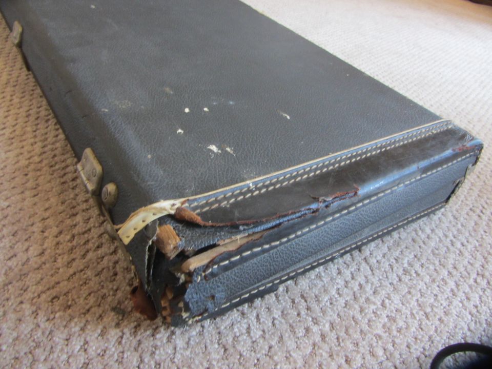 Close-up of a damaged, black, hard-shell guitar case with frayed edges and exposed wood