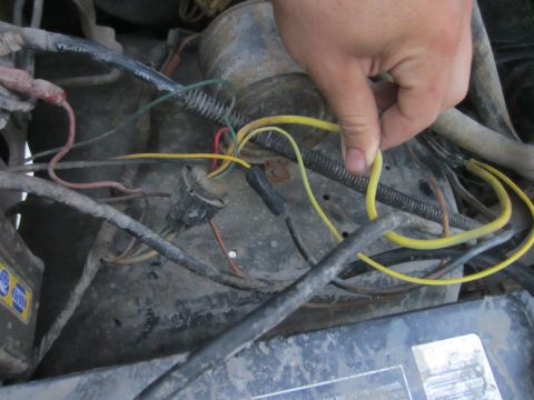 1982 Ford Bronco - Close-up of the engine bay wiring harness of a 1982 Ford Bronco, showing a hand manipulating a yellow wire.