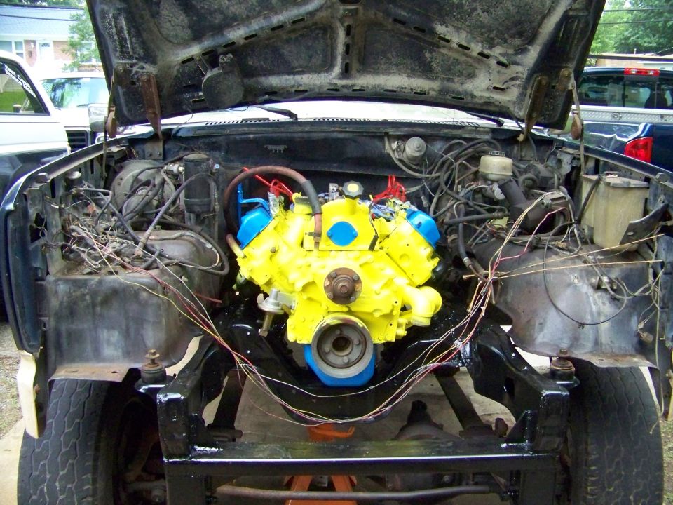Yellow V8 engine with blue parts in an open engine bay, loose wiring around it