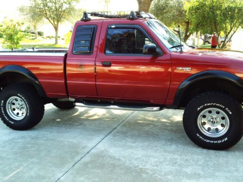 1999 Ford Ranger - A red Ford Ranger pickup truck is parked on a concrete surface, showing its side profile with aftermarket accessories.
