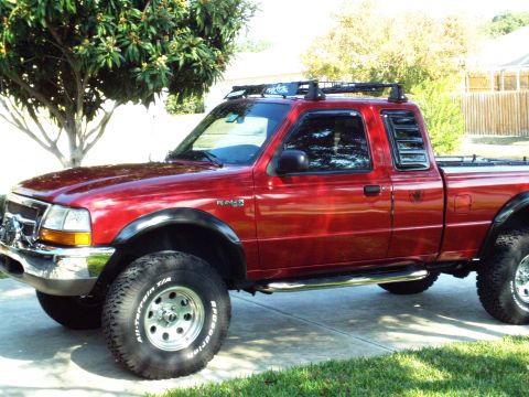 1999 Ford Ranger - This red 1999 Ford Ranger pickup truck features a roof rack and off-road tires, indicating it is ready for adventure.