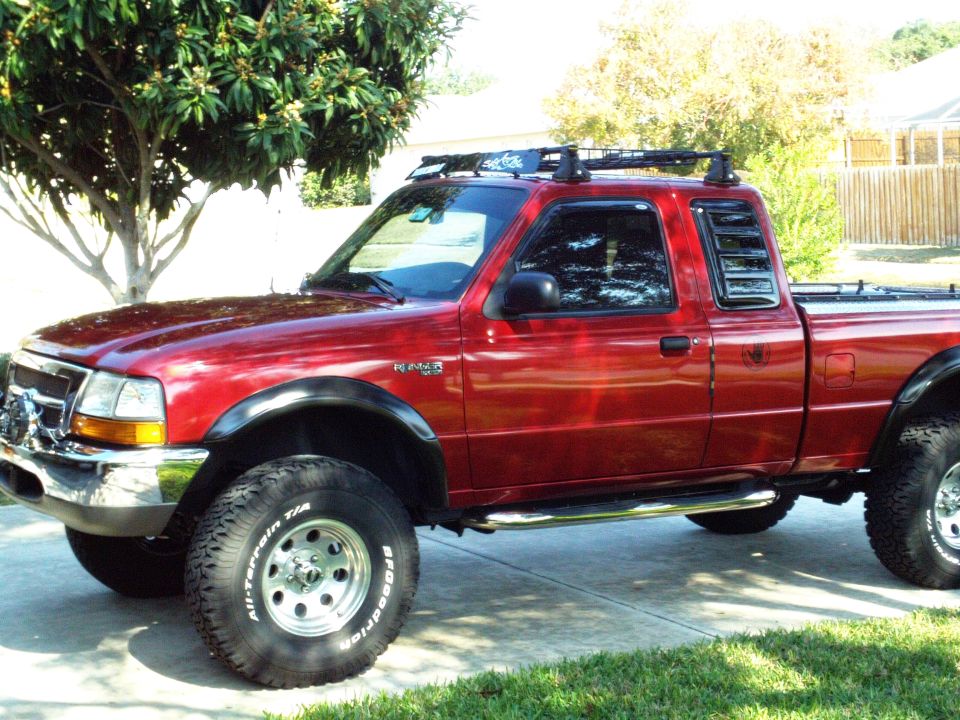 Red 1999 Ford Ranger pickup truck with roof rack and off-road tires
