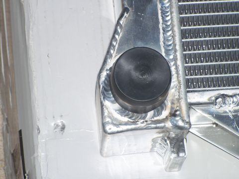1979 Ford Ranchero - Macro detail of the corner of a polished aluminum radiator, showing TIG weld beads joining the end tank and mounting bracket, with a black…