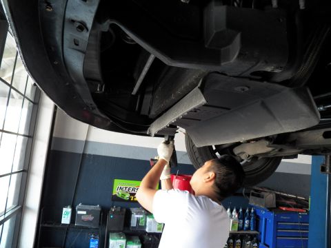 2003 Ford Crown Victoria - Technician reaches up to the undercarriage of a lifted car, oil bottles and battery rack in background.