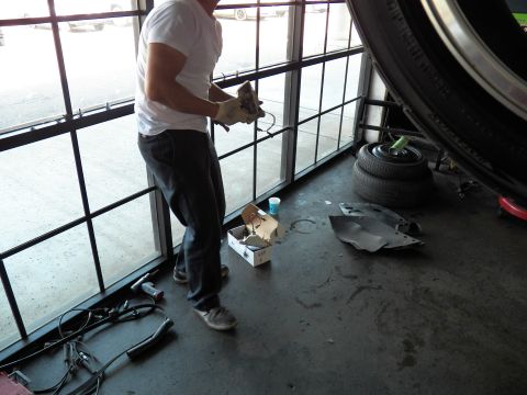 2003 Ford Crown Victoria - Technician stands by a glass roll-up door inspecting a part, tires and tools scattered on the floor.