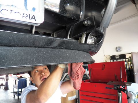 2003 Ford Crown Victoria - Front underbody of a black Crown Victoria on a lift, VICTORIA emblem above plate, worker cleaning fascia.