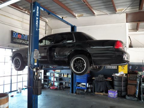 2003 Ford Crown Victoria - Black Crown Victoria elevated on a blue BendPak lift, garage shelving and tires lining the bay.