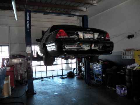 2003 Ford Crown Victoria - Backlit rear view of a Crown Victoria on a two-post lift with exhaust and tool storage below.