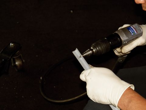 2003 Ford Crown Victoria - Close-up of gloved hands operating a tool on a slotted metal piece, rubber hose coiled nearby.