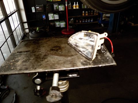 2003 Ford Crown Victoria - vehicle headlight unit rests on a worn workbench surrounded by oil shelving.