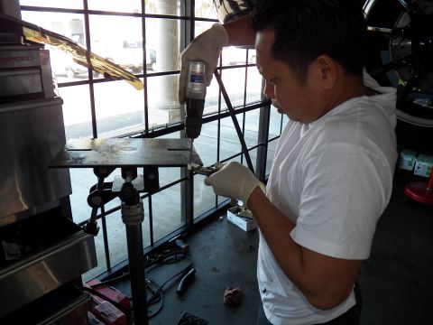 2003 Ford Crown Victoria - Gloved worker uses a power drill on a bracket secured to a stand in a service bay.