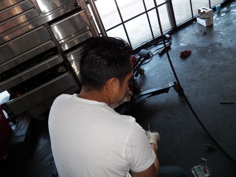 2003 Ford Crown Victoria - Technician kneels near a stainless toolbox and floor parts inside an open shop bay.
