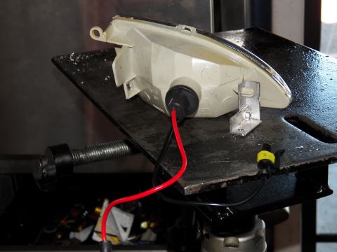 2003 Ford Crown Victoria - headlight shell with attached wiring sits on a black metal work surface and bolt.