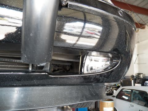 2003 Ford Crown Victoria - View of a dark vehicle front bumper and clear fog lamp inside a service garage.
