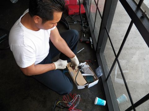 2003 Ford Crown Victoria - Technician attaches leads to a lighting ballast resting in a box on the concrete.