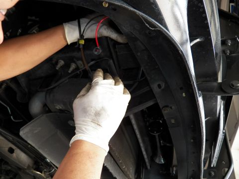 2003 Ford Crown Victoria - Technician guides a wiring lead behind the inner fender of a vehicle on a lift.