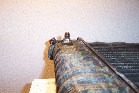 1980 Ford Bronco - A close-up view of a rusty radiator, showing a brass fitting and a red cap.