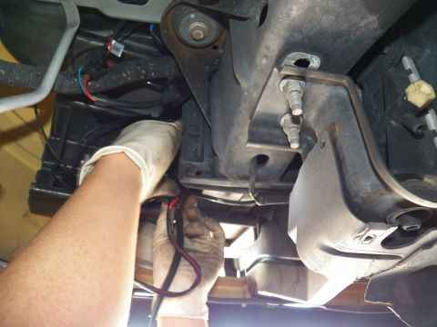 2003 Ford Crown Victoria - Technician in latex glove guiding a red lead along the chassis crossmember beneath a raised vehicle