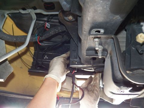 2003 Ford Crown Victoria - Mechanic feeds red and black wiring through a frame gap near a black bracket beneath the car