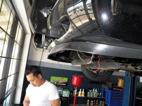 2003 Ford Crown Victoria - View under a black sedan's rear bumper on a shop lift, Interstate Batteries display in background