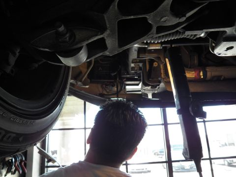 2003 Ford Crown Victoria - Worker views the underside drivetrain and suspension of a raised vehicle next to its rear tire