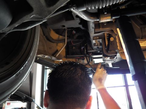 2003 Ford Crown Victoria - Technician works overhead on the underside of a raised car beside the tire and chassis members