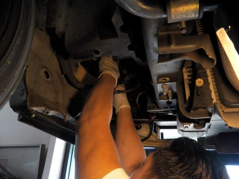 2003 Ford Crown Victoria - Mechanic reaches deep into the chassis of a lifted vehicle among frame and suspension parts