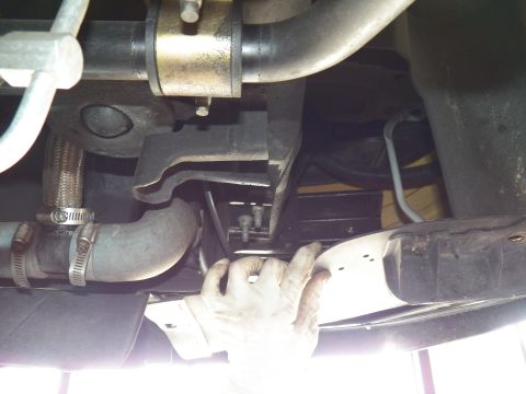 2003 Ford Crown Victoria - Hand steadies a metal panel beneath braided hose, clamps and exhaust piping of a raised vehicle