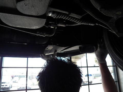 2003 Ford Crown Victoria - Drivetrain and undercarriage of a lifted vehicle with a worker reaching up beside the rear tire