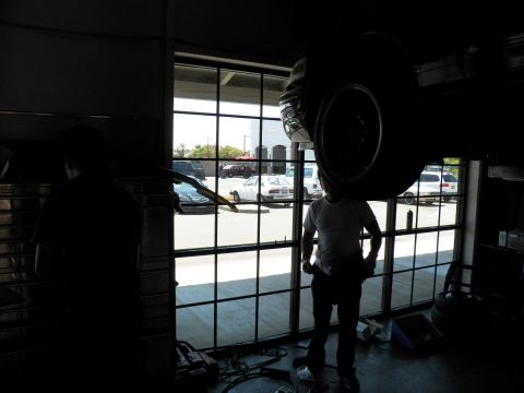 2003 Ford Crown Victoria - Backlit garage scene showing a lifted vehicle wheel and workers against the shop bay windows