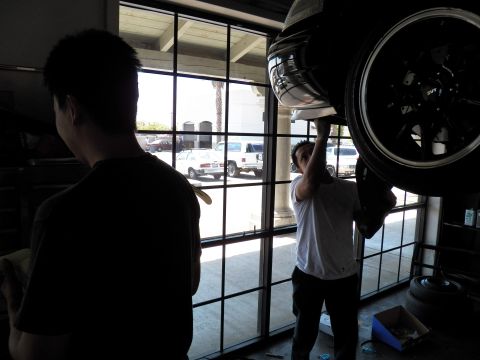 2003 Ford Crown Victoria - Worker reaches to a multi-spoke wheel on a raised car while another person looks on in the garage