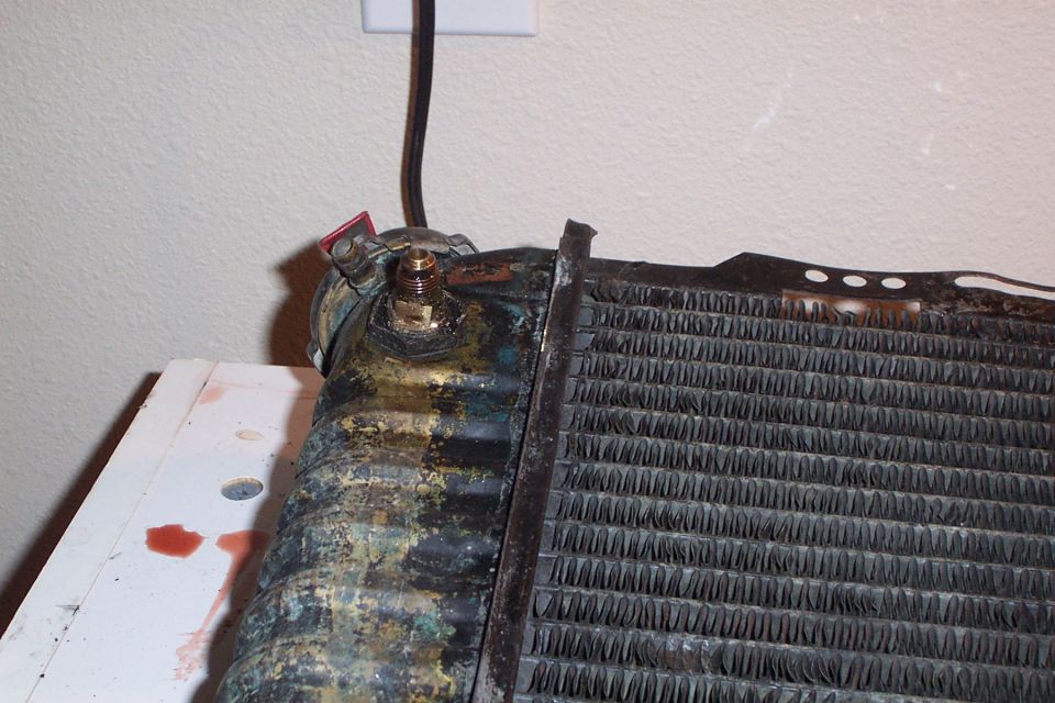 Close-up of a corroded radiator with red fluid drips on a white surface