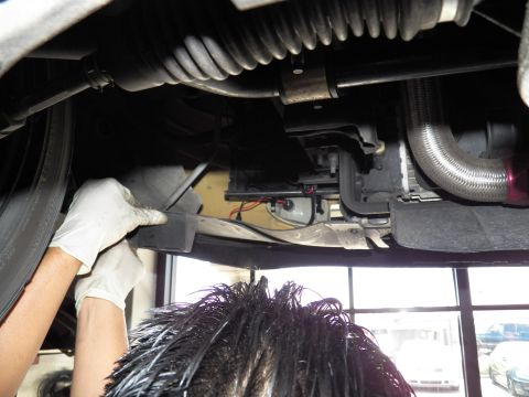2003 Ford Crown Victoria - View under a raised car of the steering rack, braided line and tank as a technician reaches up