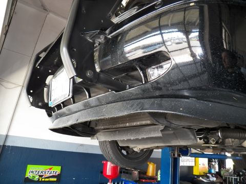 2003 Ford Crown Victoria - Underside of a black sedan's front end on a shop lift with an Interstate Batteries display below