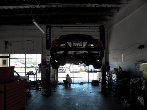 2003 Ford Crown Victoria - Rear view of a black sedan elevated on a shop lift as a technician kneels under it in the bay