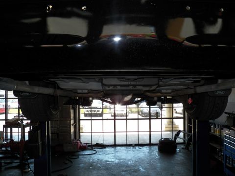 2003 Ford Crown Victoria - Front undercarriage of a lifted black Ford sedan, looking out toward the shop's glass bay door