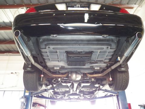 2003 Ford Crown Victoria - Black car raised on a shop lift, underbody view of dual exhaust outlets, rear subframe and Ford-logo mud flaps.
