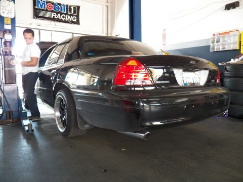 2003 Ford Crown Victoria - Worker stands by the open hood of a black Crown Victoria seen from the left rear